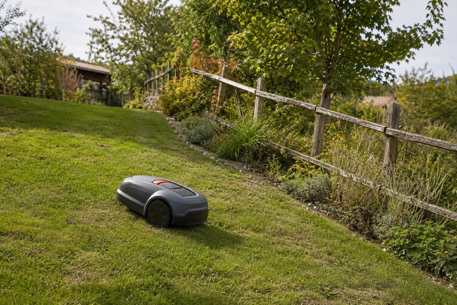 Robot tondeuse travaillant sur une pelouse en pente le long de la limite du terrain